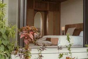 A minimalist bedroom featuring a wood frame bed with a white quilt and pillows, surrounded by green plants.