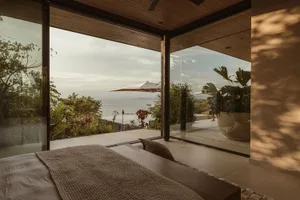 A minimalist bedroom with glass windows overlooking natural scenery and a sea view.