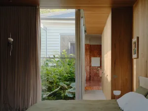 A minimalist bedroom featuring wooden walls, plants, and a neatly made bed.