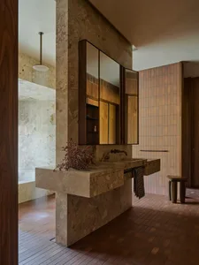 Modern bathroom featuring a marble sink and walls, with a wooden cabinet and a shower area visible in the background.