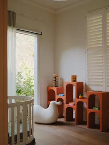 A modern children's bedroom featuring white furniture with bird-shaped armé and orange modular shelving units with children's