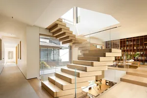 Modern floating staircase with wooden steps and glass railings, leading to a second floor.