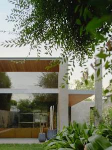 Modern frontyard with concrete pillars and glass walls surrounded by lush greenery.