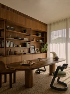 A modern home office with wooden furniture, a large oval table, and a bookshelf.