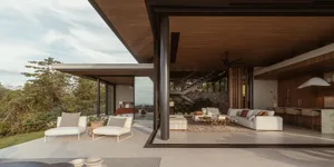 Modern residential living room featuring a wooden ceiling, white sofas, and lush greenery outdoors.