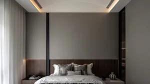 A stylish, minimalist bedroom with a bed against a large, wooden-walled backdrop, featuring grey and white bedding and decora