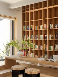A minimalist home office with wooden furniture, glass shelving, and a large bookshelf filled with colorful books.