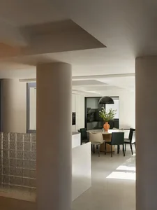 A modern kitchen with white cabinets, a transparent glass divider, and a round dining table.