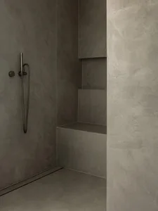 A minimalist bathroom with concrete walls and floors, featuring a modern shower area with a hand shower head and built-in she