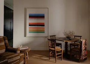 A minimalist living room with reclaimed wood furniture, a colorful abstract painting on the wall, and a small dining area wit