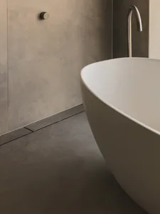 Modern bathroom featuring a white ceramic bathtub with a sleek, minimalist design and concrete tiles on the floor and walls.