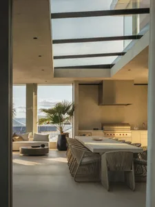 Modern dining room with concrete and glass materials, featuring an outdoor kitchen and skylight.