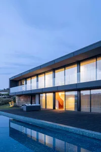 Modern residential house with glass walls and stone accents, featuring a swimming pool.