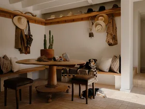 A rustic living room with wooden furniture, a round table, cushions, a cactus plant, and a dog.