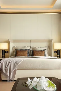 A modern bedroom featuring a bed with white bedsheets and pillows, accompanied by a glass table with orchid flowers.