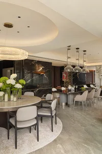Modern dining room featuring a round marble table and chairs, alongside a bar area with pendant lights and wine storage.