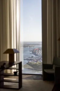 A modern hotel room with a view through transparent glass curtains, featuring leather furniture and a serene waterfront setti