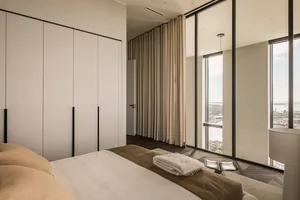 Contemporary bedroom with neutral tones and large windows overlooking a scenic view.