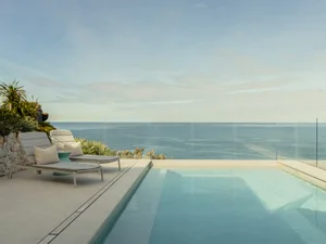 A modern waterfront swimming pool with a glass wall overlooking the ocean.