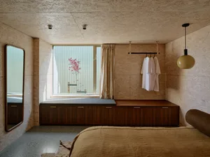 Minimalist bedroom with concrete floor, wooden bench, and hanging garments