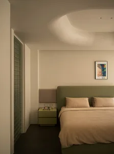 Minimalistic bedroom featuring a green upholstered bed with neutral textiles and a sleek nightstand.