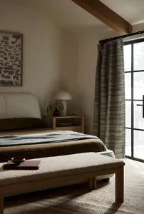 Minimalist bedroom with a bed, bench, side table, and textured cotton blend drapes hanging in front of a window.