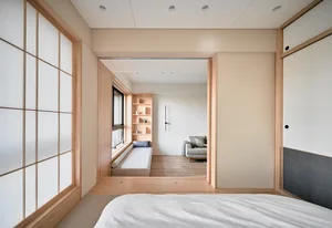 A minimalist bedroom featuring wood furnishings, fabric bedding, and plaster walls.
