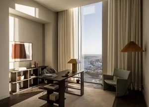A minimalist office with wooden furniture and marble flooring, featuring a large window with a city view.
