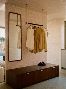 A modern closet with a wooden bench, jacket hanger, and mirror against textured wooden panels.