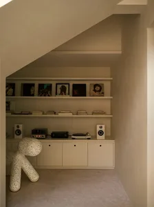 A modern music room with a concrete floor, shelves displaying framed album covers and books, and a white audio speaker.