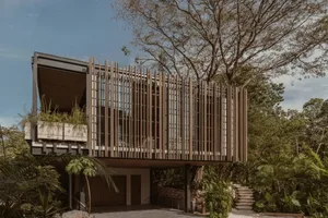 A modern house with a wooden exterior featuring large glass windows and a balcony surrounded by lush greenery.