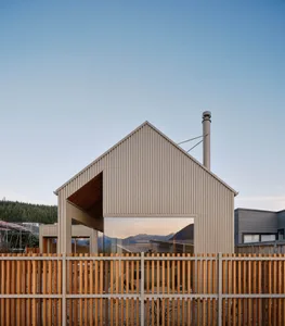 A modern house with a corrugated metal exterior and a large window reflecting the sky and surrounding landscape.