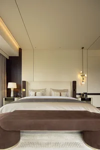Modern minimalist bedroom featuring a bed with white and beige textiles and a brown upholstered bench.