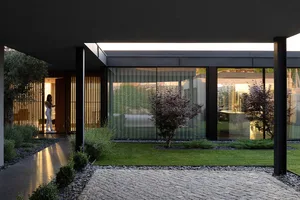 A modern minimalist house featuring glass, concrete, and a neatly maintained lawn.