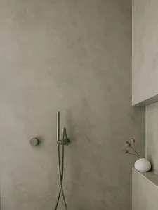 A minimalist bathroom with concrete walls and a hand-held shower head.