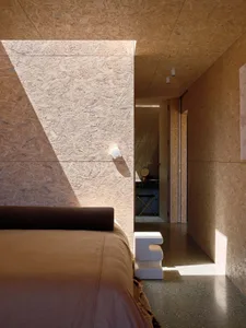 A minimalist bedroom featuring OSB board walls and a sleek, modern bed