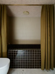 Modern bathroom with black tiled walls and floor, featuring a white toilet and beige tiled ceiling.