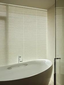 A modern bathroom with a white bathtub, blinds, and ceramic tiles.