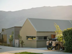 A modern house with a metal siding exterior and a classic off-road vehicle parked nearby. The building sits against a backdro