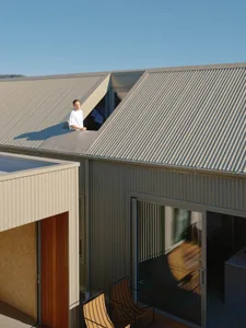 A person standing on the rooftop of a modern house with a corrugated metal roof.