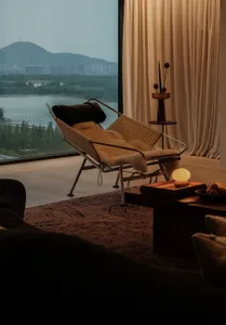 Contemporary armchair with wooden frame and faux fur blanket, situated in a modern living room with a cityscape view.