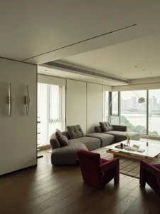 A modern living room featuring a fabric sectional sofa, glass windows, and wooden flooring with a ceiling light fixture.