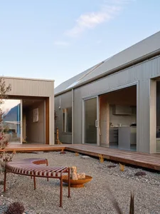 Modern house with a metal-clad exterior and a gravel courtyard with a fire pit and bench.