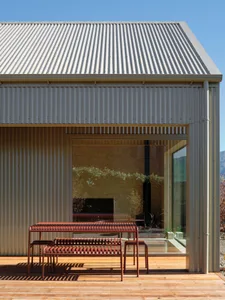 A modern home with a corrugated metal exterior and wooden patio furniture.