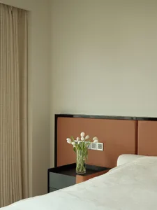 Modern minimalist bedroom featuring a bed dressed in cotton sheets and a leather headboard, with a wooden nightstand and a va