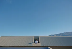 A person standing on a corrugated metal roof overlooking a mountain view under a clear blue sky.