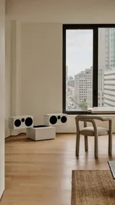 Minimalist living room with wood flooring, a beige armchair, and modern audio speakers.