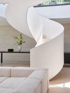 A modern living room with white concrete walls, a spiral staircase, and a white sofa.