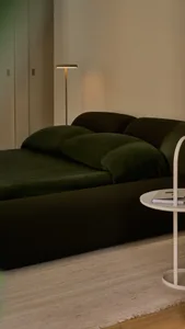 A minimalist bedroom featuring a green velvet bed and a floor lamp.