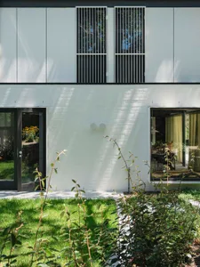 Modern residential exterior with white brick walls, metal cladding, large windows, and glass doors.